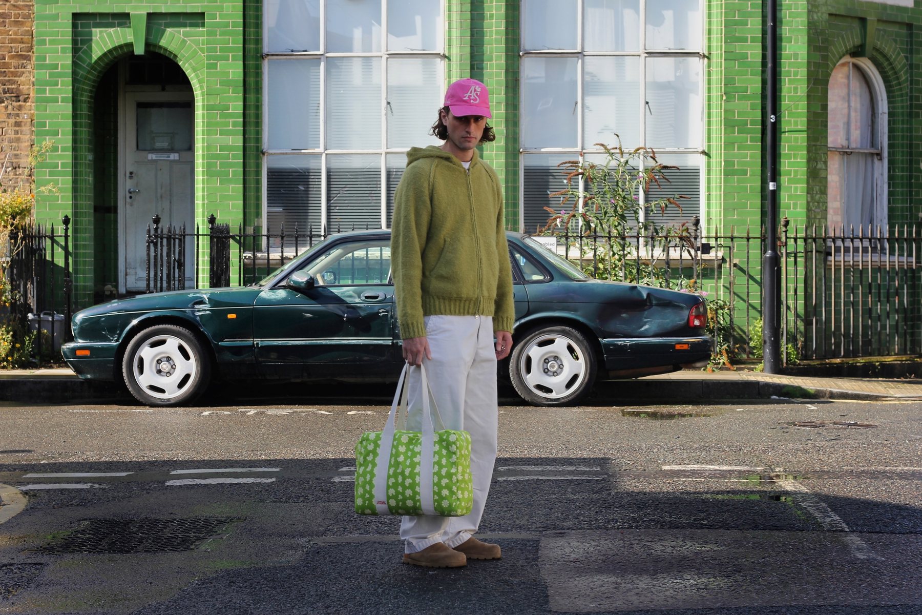 Model in a pink AS cap holding a green floral Affair Studios bag on a London street